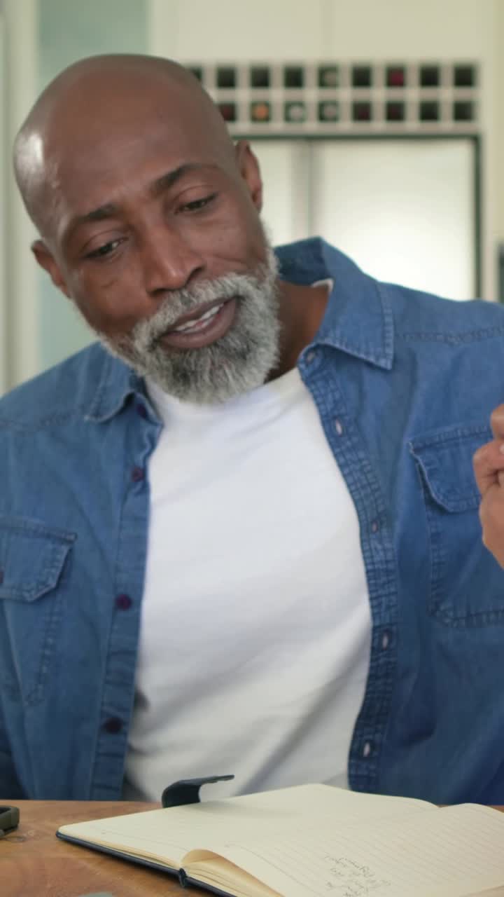 Video verticale: un anziano con camicia di jeans guarda appunti e telefono a casa, rispondendo
