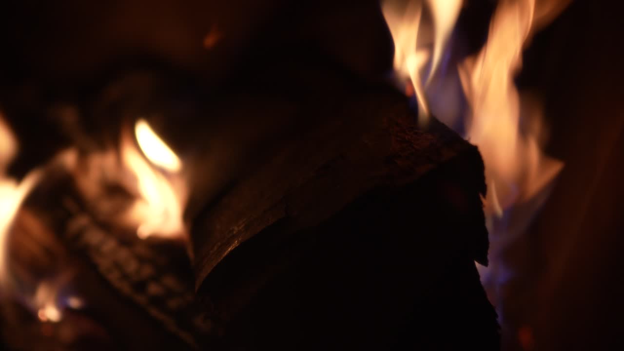 Blurry flames dance around logs in a dark cozy fireplace indoors