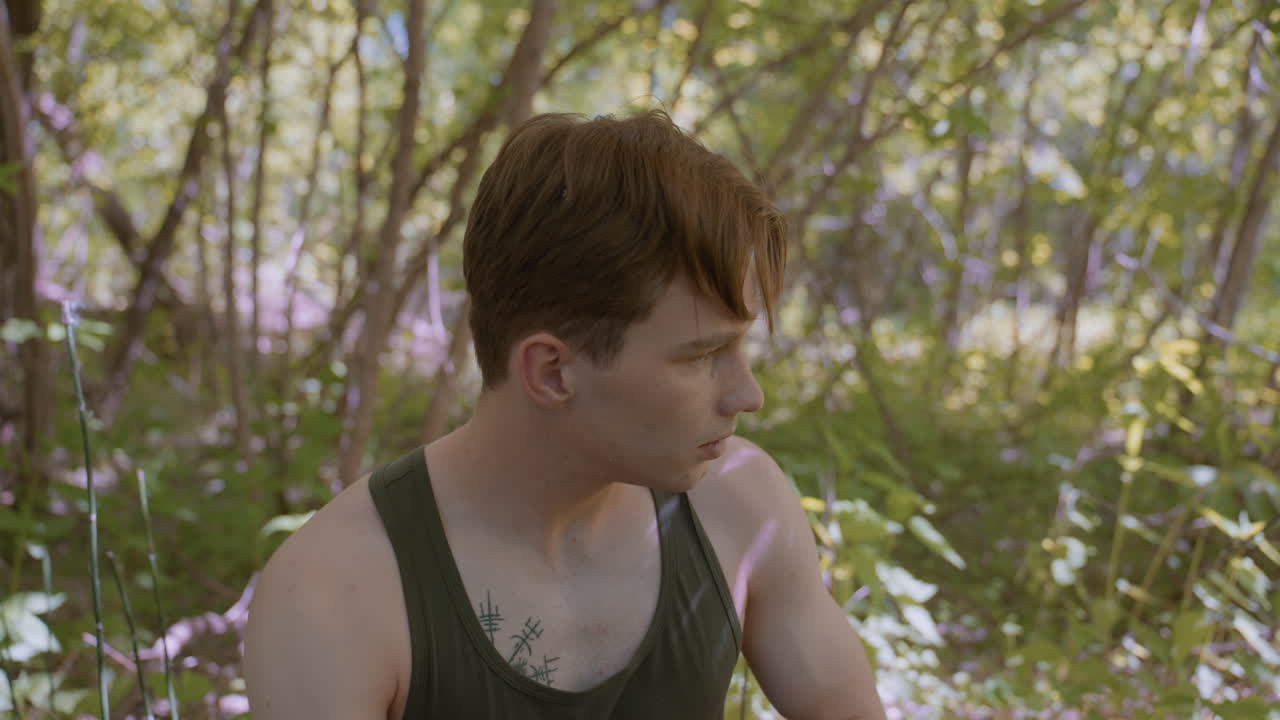 Adventurer loosens headband to tie it better, with sunlight reflecting on the shoulder and off surrounding trees, in a peaceful forest setting, preparing for the next stage of the journey