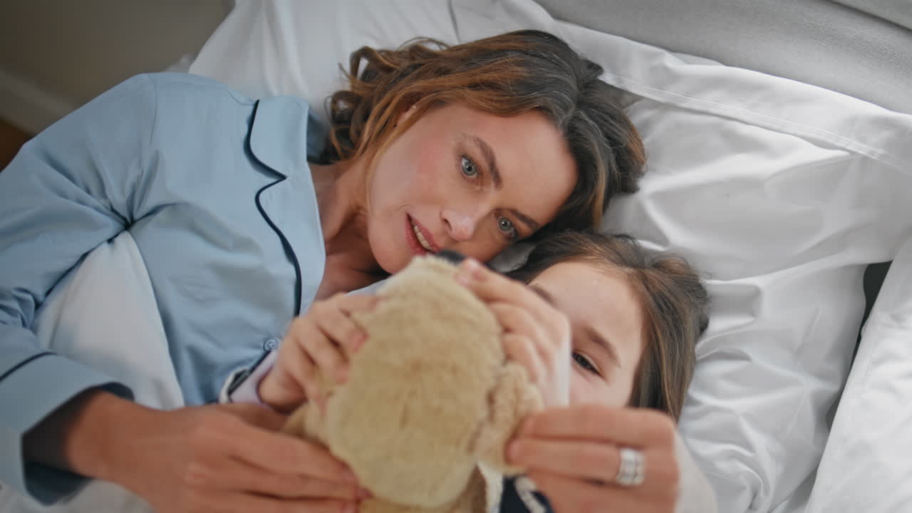 Bambina e madre giocano in una camera da letto accogliente, primo piano. Donna e bambina giocano con un orsacchiotto