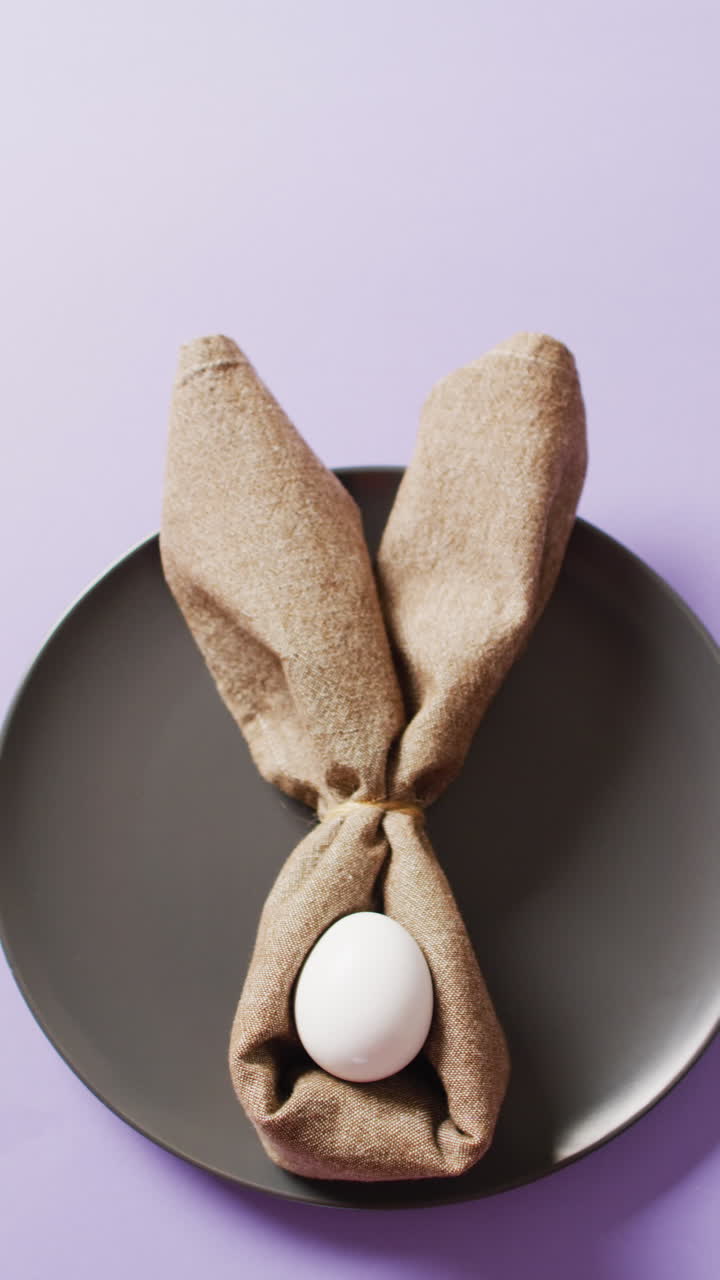 Vertical video of egg and ribbon in shape of rabbit on plate on purple background with copy space