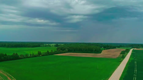 Campos-Verdes-Vibrantes-Bajo-Un-Cielo-Tormentoso,-Resaltando-Los-Contrastes-De-La-Naturaleza,-Vista-Aérea