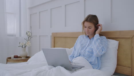 woman working laptop computer on bed. happy pretty female working from home on key laptop computer from bedroom.