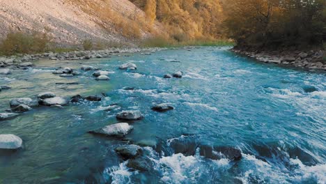 a low flight over a small waterfall and a mountain river, and crystal turquoise stones among the mountains. in the background, tourists are photographed. sunset time. the sun's rays give orange flare. the concept of freedom of leisure, vacation