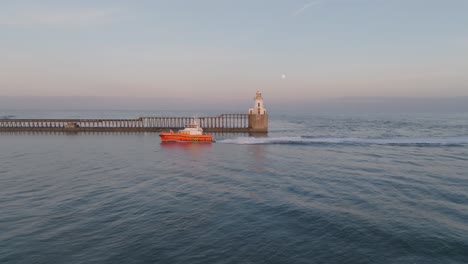 orange tugboat entering harbour at sunset