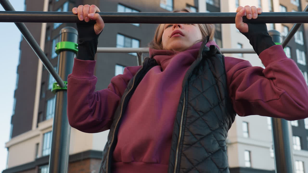 Female athlete working out on horizontal pull up bar in park with autumn foliage backdrop demonstrating forearm strength control and focus during intense calisthenics on rubber flooring