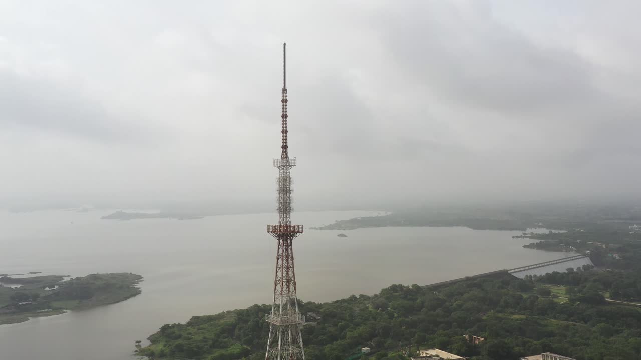 Aerial View of a Tall Communication Tower Near a Lake on a Cloudy Day