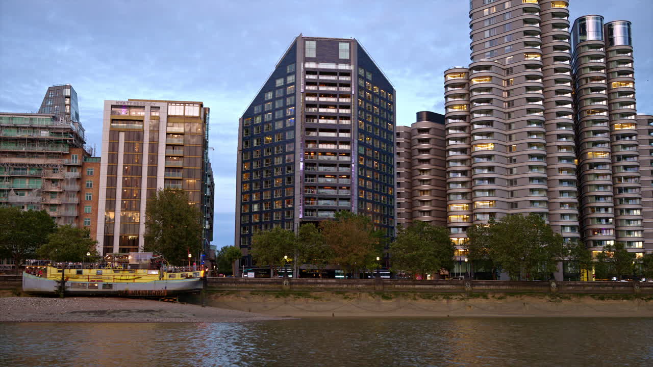 View of London from a floating boat on the Thames River at sunset, United Kingdom. Modern residential buildings located on the embankment street along the river