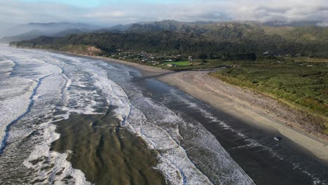 aerial view of rapahoe beach with vehicles driving and waves breaking on sandy shore. west coast, new zealand. pullback shot
