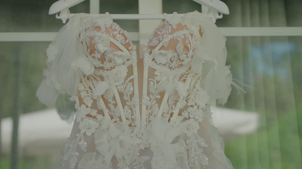 꽃으로 장식 된 세부적인 렌즈 웨딩 드레스 가 창문 에 매달려 있어, 특별한 날 에 신부 를 기다리고 있다