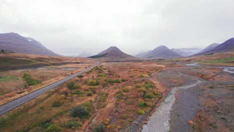 Luftaufnahme:-Schwenk-Von-Links-Nach-Rechts-Der-Isländischen-Ringstraße,-Einer-Malerischen-Autobahn-Durch-Ein-Malerisches,-Abgelegenes-Fjordgebiet,-Das-Zu-Zwei-Gipfeln-Mit-Nebel-Und-Dunst-In-Der-Ferne-Führt