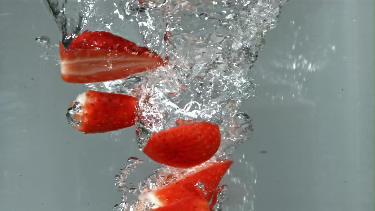 Fragole rosse fresche e fette che cadono nell'acqua al rallentatore
