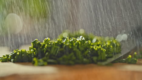 Primer-Plano-De-Cebolletas-Frescas-Picadas-Sobre-Una-Tabla-De-Cortar-De-Madera,-Luego-Se-Rocía-Agua-Sobre-Ella