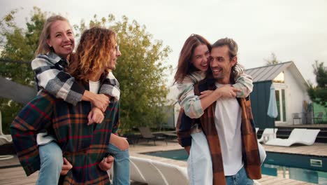 Two-girls-are-sitting-on-their-boyfriends'-backs-in-checkered-shirts-near-the-sunbeds.-Rest-in-the-country-house