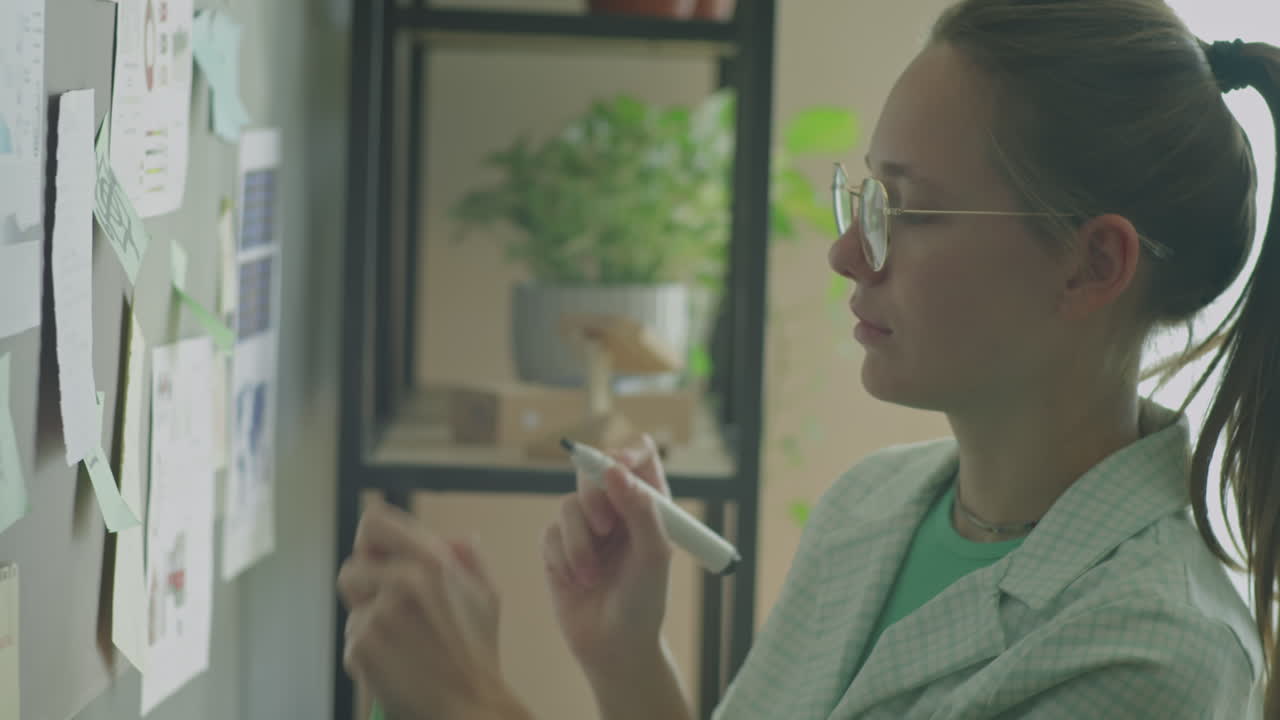 Gen Z Girl Writing on Sticky Notes Attached to Wall in Office