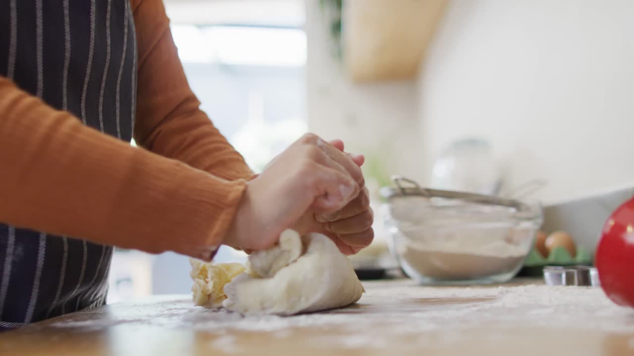 video de la mitad de la mujer biracial horneando en la cocina en casa, amassando masa en la encimera.