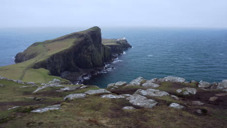 toma de seguimiento del faro de neist point con acantilados rocosos en primer plano y el océano atlántico en el fondo en un día ventoso y nublado en escocia, isla de skye