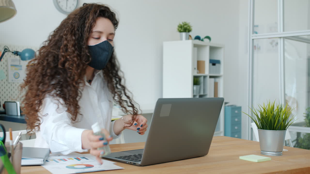 Woman sanitizing hands during a video call in the office