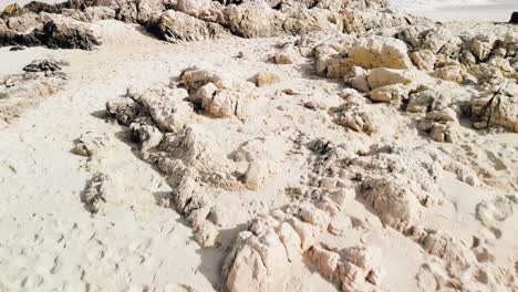 low aerial drone shot starting over some white rocks and panning up to clear blue water of the mediterranean at a beach in majorca