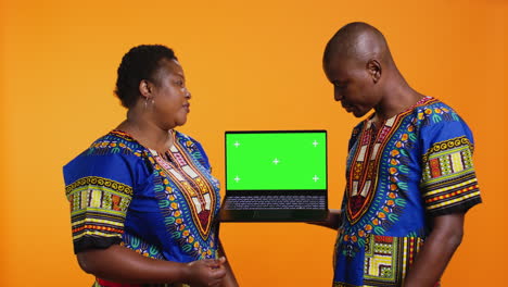 ethnic couple showcasing laptop with greenscreen display