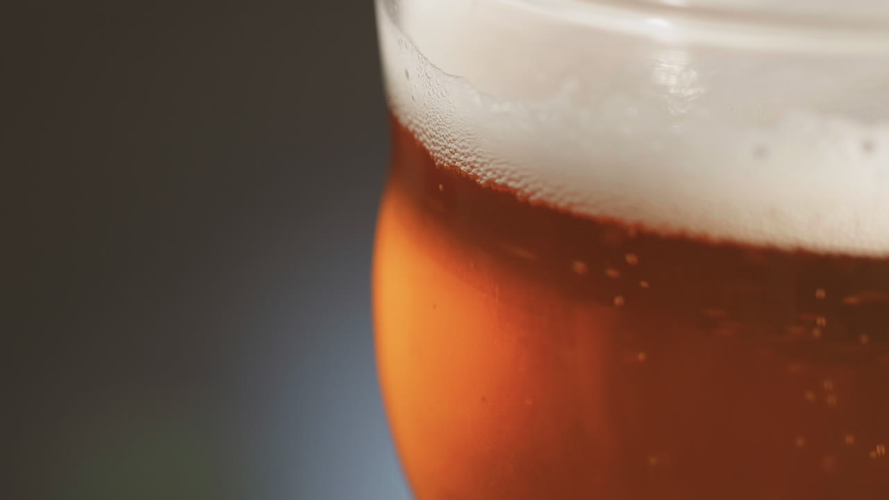A curved pint glass with beer and bubbles rising up to the foam head, copy space