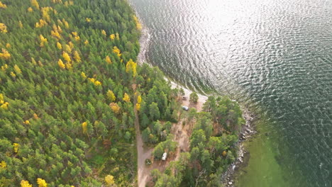 Schweden-–-Bezaubernde-Herbstlandschaft-Mit-Birken--Und-Tannenwäldern-Entlang-Des-Küstenmeeres,-Ein-Platz-In-Der-Natur,-Wo-Camper-Parken-Können-Und-Die-Sonnenstrahlen-Die-Szene-Erhellen-–-Luftaufnahme-Mit-Einer-Drohne