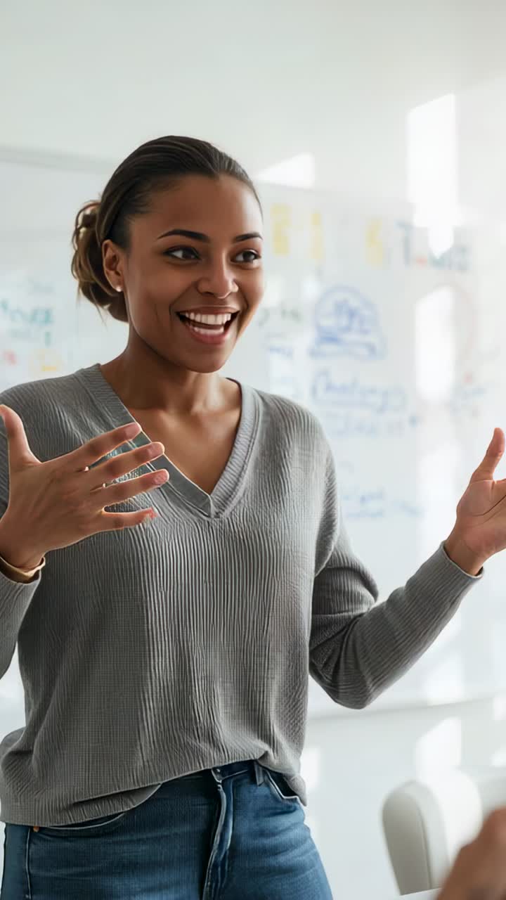Vertical video: Starting talk woman in gray sweater, explaining diagrams in room, with whiteboard