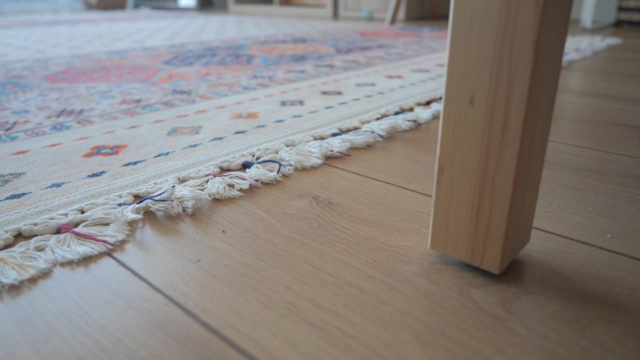 Primo piano di una gamba di tavolo in legno su pavimento in parquet con tappeto a motivi
