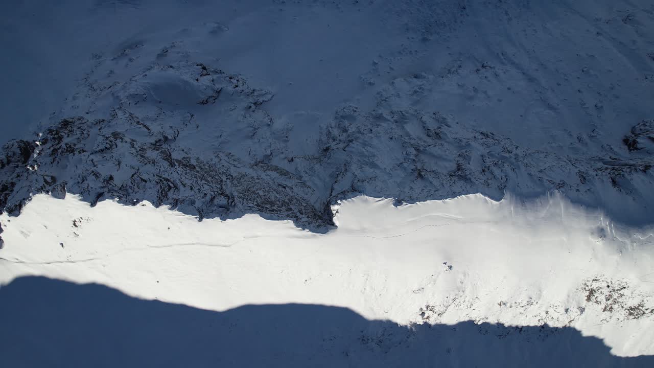 Winter peaks above drifting clouds under clear sky. Alpine drone view in crisp sunlight