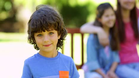 niño agitando a la cámara con la familia detrás en el banco del parque