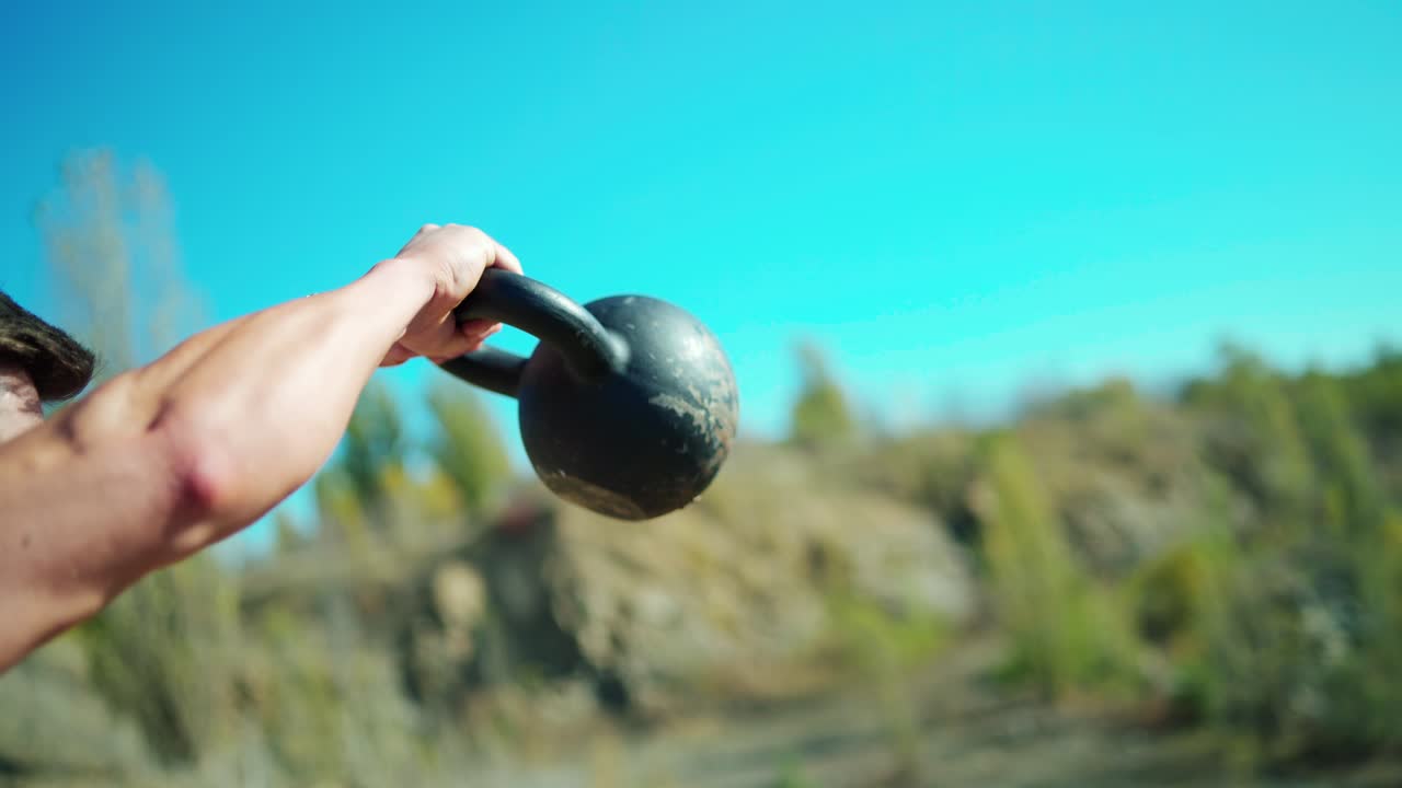 Bodybuilders training among nature. Heavy kettlebell in man's arms during workout. Athletic men lifting weights. Close-up.