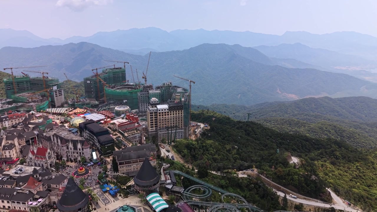 Ba Na Hills SunWorld tesisi, binaları ve cazibe merkezleriyle yukarıdan, Vietnam'da berrak bir gökyüzünün altında yemyeşil dağlarla çevrili olarak görülüyor