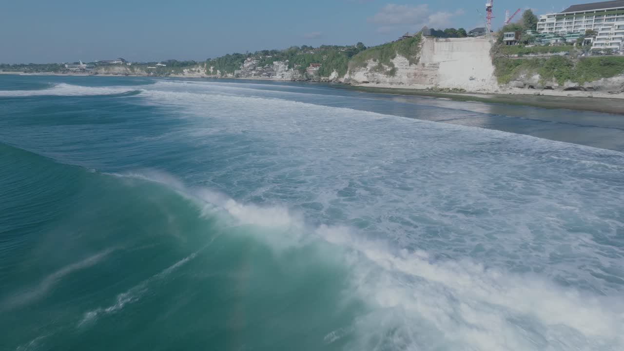 Ripresa con drone dal basso di surfisti e onde blu con distruzione ambientale sullo sfondo a Uluwatu, Bali, Indonesia