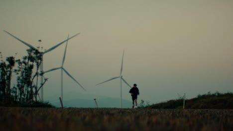 man running at sunset by windmills