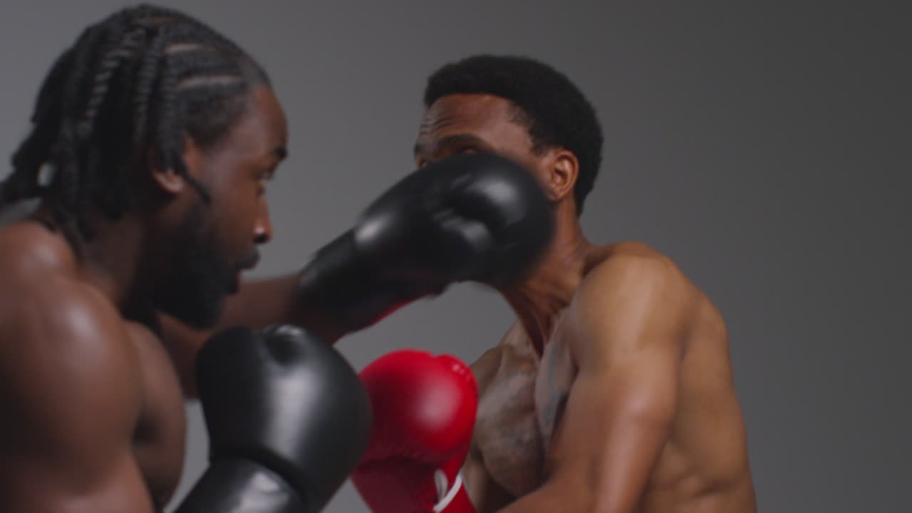 fotografía de estudio de cerca de dos boxeadores masculinos con guantes luchando en un partido de boxeo contra un fondo gris
