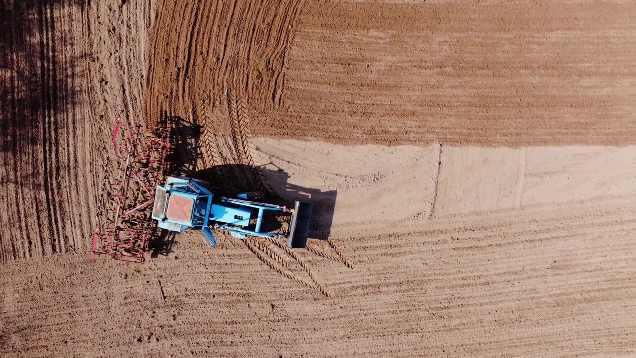 Droneoptagelse ovenfra følger traktor, der bearbejder jorden, efterlader mønstre, landbrugsjord