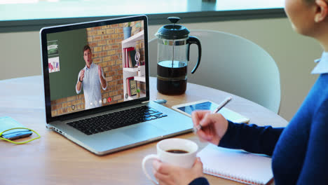 Caucasian-female-student-using-laptop-on-video-call-with-male-teacher,-making-notes