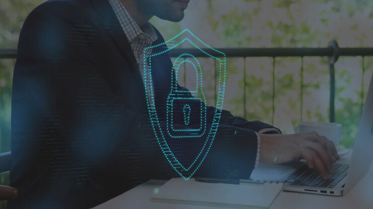 Animation of padlock in shield over biracial man drinking coffee and working on laptop