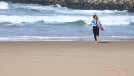 rear view of mixed race woman running from beach into the sea carrying surfboard