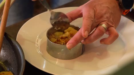 person spoons potatoes, onions from skillet onto plate, preparing for serving.