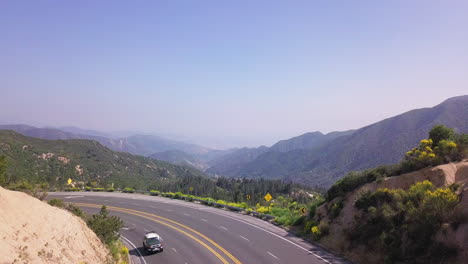 Drone-flight-above-winding-asphalt-road-with-picturesque-mountainous-landscape-in-background