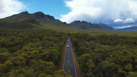 4k drone video flying forward through lush green nature following a white camper van driving towards the grampians national park in victoria, australia