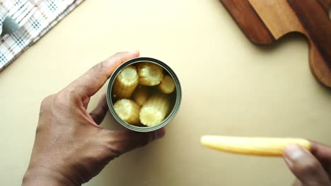 closeup of a hand holding a can of canned corn, preparing food in a kitchen