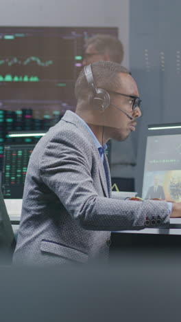 multiethnic financial analysts, businesspeople monitor real-time stocks on computer, work in bank office. big digital screen with tv news broadcast and exchange market charts on background. vertical