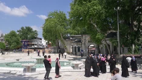 people walking by a fountain in front of a mosque in istanbul