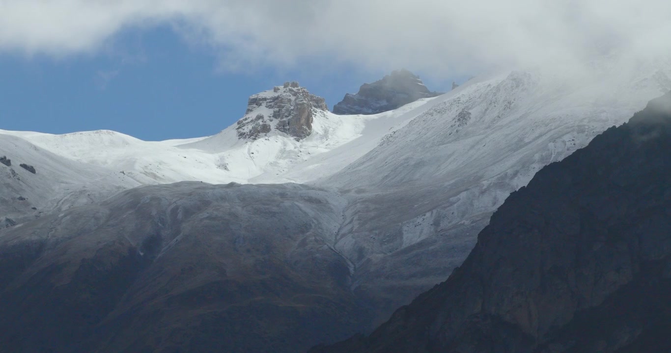 Movimento laterale di un drone aereo che sorvola un ripido pendio roccioso scuro per rivelare una cresta innevata sotto un cielo blu nel Mustang, Nepal