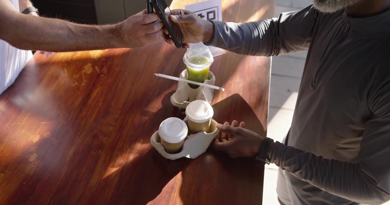 Due uomini che scansionano un codice QR, mostrano i telefoni, ritirano bevande e caffè al tavolo di ritiro, con spazio per il testo