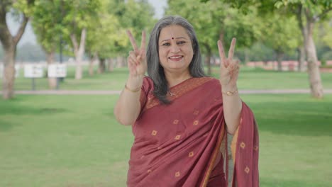 una anciana india feliz mostrando el signo de la victoria en el parque