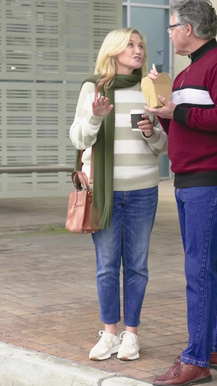 Vertical video: Lifting food, man offering takeout with chopsticks at plaza, woman sipping coffee