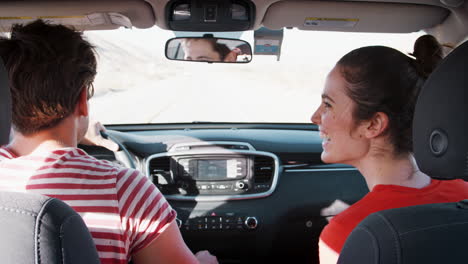 una pareja blanca bailando en el coche mientras conducen, vista trasera